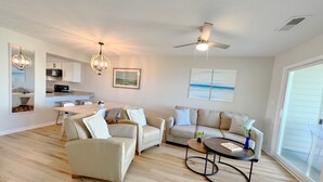 A spacious living room with a dining area, a kitchen, and a large window. - BEACHFRONT:3 BR, 2 Full BA, Renovated, Beach Access , BBQ, Pool, Sleeps 9 (Oak Island)