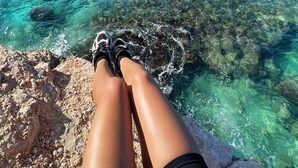 A person sitting on a rocky outcrop overlooking turquoise waters and a clear sky.