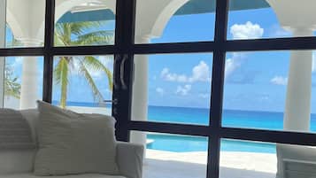 A room with a large window overlooking a beach, a white sofa, a wooden coffee table with a remote control, and a pair of sneakers.