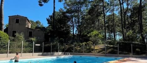 A swimming pool with a tiled deck, surrounded by trees and a fence.