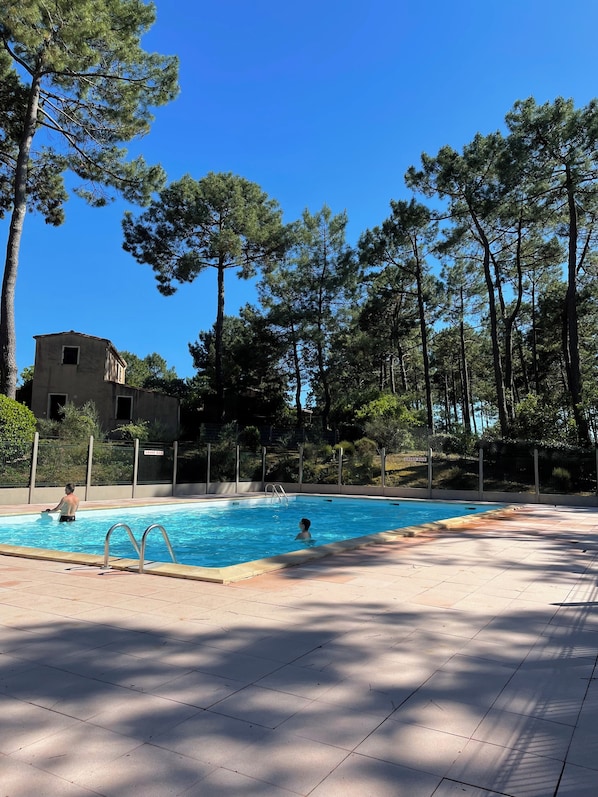 A swimming pool with a tiled deck, surrounded by trees and a fence. - Stunning TERRACE, house with ALL MOD CONS NEAR THE BEACH, SWIMMING POOL, QUIET. View of the Forest (Lacanau)