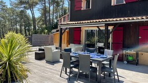 A wooden deck with outdoor furniture, a dining table, and red shutters on the building.