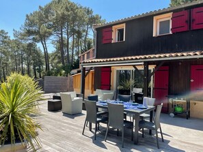 Une terrasse en bois avec des meubles d’extérieur, une table à manger et des volets rouges sur le bâtiment.