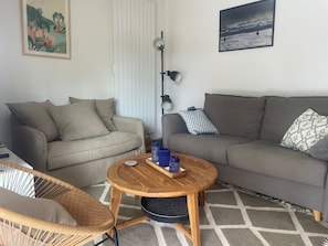 A living room with a sofa, a round wooden coffee table, a wicker chair, and a floor lamp. - Superb TERRACE, house ALL COMFORT NEAR BEACH, SWIMMING POOL, PAISIBLE. Forest view (Lacanau)