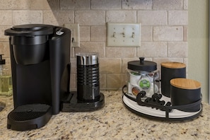 A kitchen with a coffee maker, a grinder, a coffee storage container, and a tray with mugs.