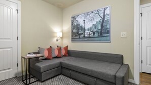 A corner living room with a gray sectional sofa, a small side table with a lamp, and a patterned rug.