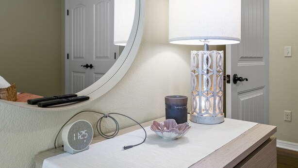 A bathroom vanity with a mirror, a lamp, a candle, and a clock.