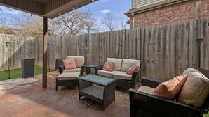 An outdoor patio with wicker furniture, a covered area, and a wooden fence.