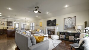 A spacious living room with a gray sofa, a fireplace, a television, and a dining area.