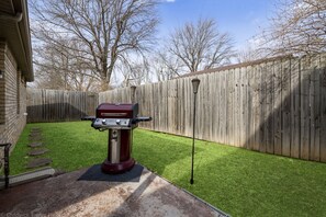 A backyard with a barbecue grill, a wooden fence, and a paved patio.