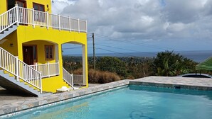 Un bâtiment jaune avec une piscine, des escaliers et une vue sur l’océan.