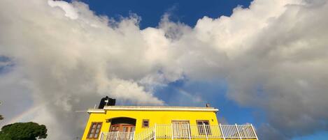 A two-story yellow building with a balcony and a water tank on the roof.