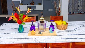 Une table à manger avec une bouteille de spiritueux, des objets de décoration et un panier de fruits.