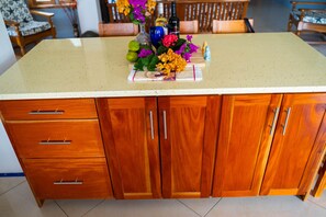 Une cuisine avec des meubles de rangement en bois, un plan de travail à motifs et un vase rempli de fleurs.