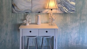 Ein Zimmer mit einem weißen Schreibtisch, zwei Metallhockern, einer Lampe und einem großen abstrakten Gemälde an der Wand.