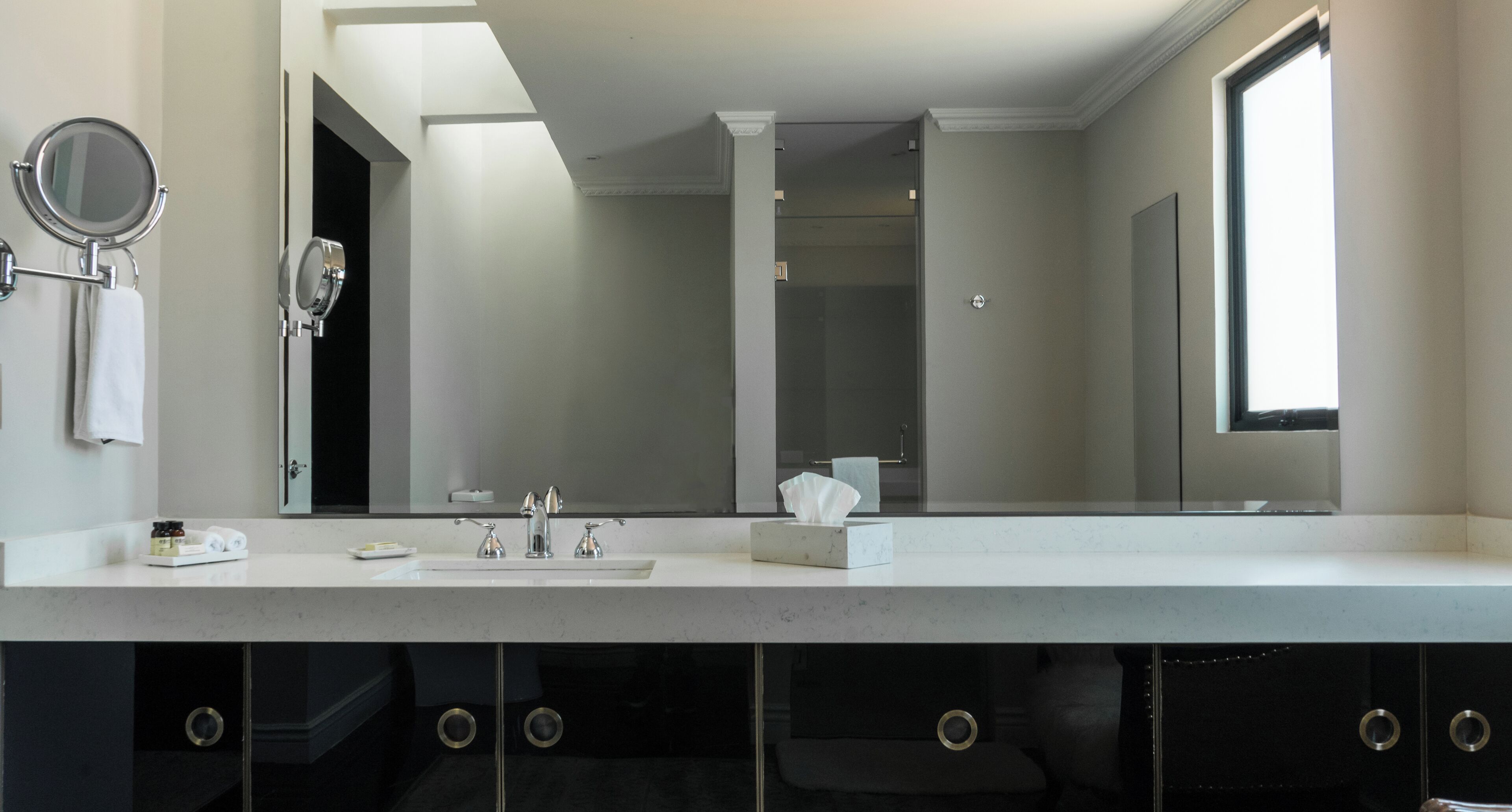 Un baño moderno con un espejo grande, un lavamanos y una ventana.