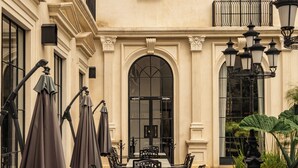 Un patio al aire libre con mesas y sillas, un amplio arco de entrada y un balcón con barandilla.
