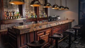 Una zona de bar con mostrador de mármol, taburetes de madera y una variedad de botellas de licores.