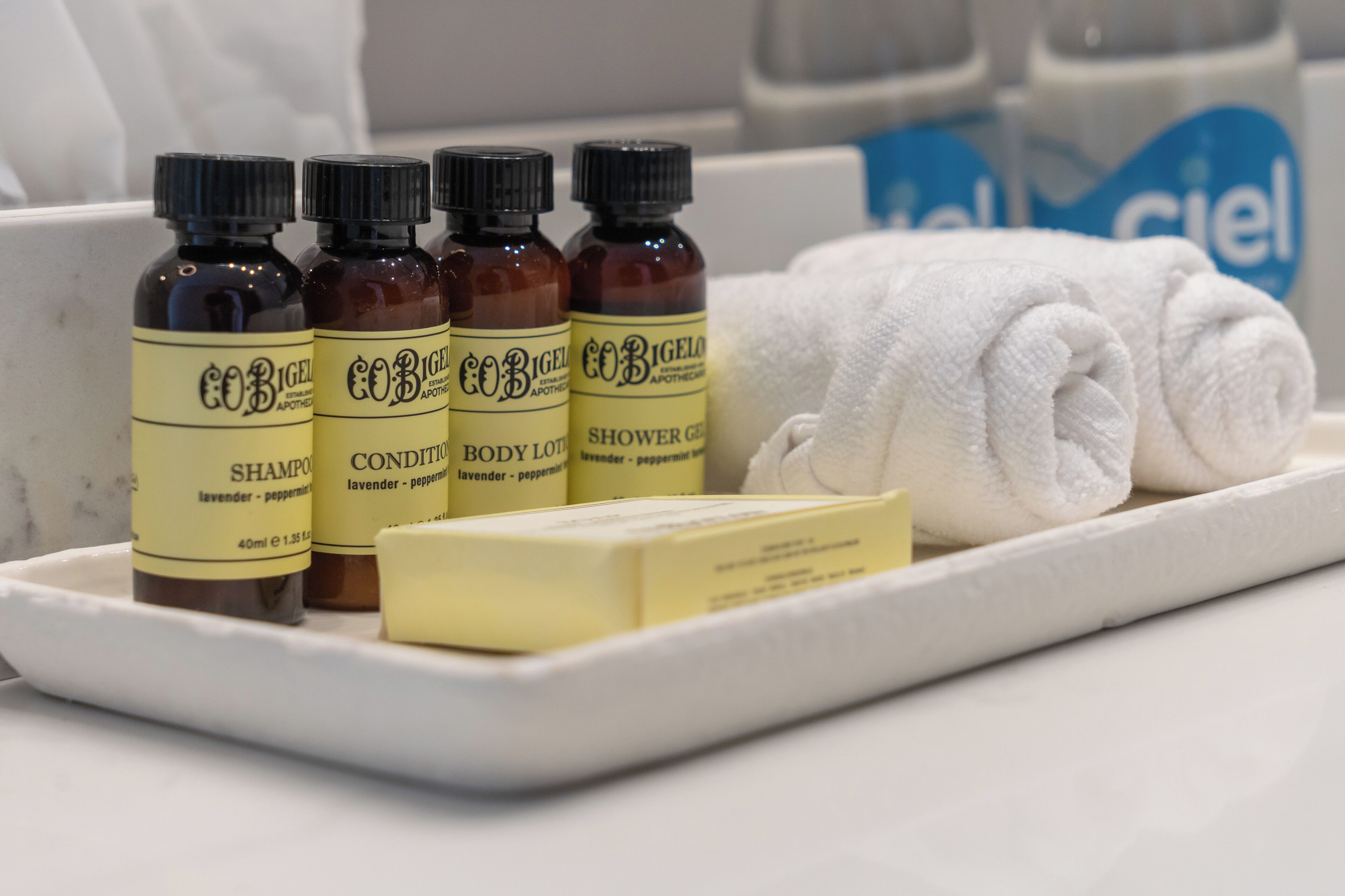 A tray with three bottles of body lotion, a bar of soap, and a rolled white towel.