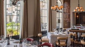 Comedor con mesas dispuestas para una comida, ventanas amplias con cortinas y candelabros colgantes.