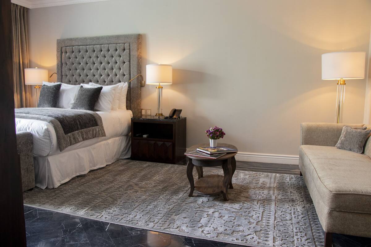 A hotel room with a large bed, a sofa, a small table with a vase, and two bedside lamps.