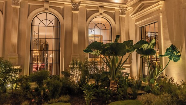 Un patio de hotel con amplias ventanas arqueadas, una planta central y un jardín bien cuidado.