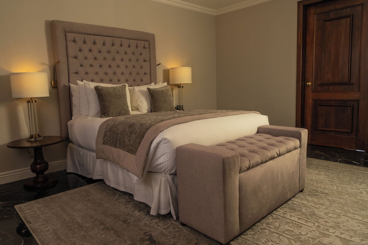 A bedroom with a large bed, two bedside lamps, a wooden door, and a marble floor.