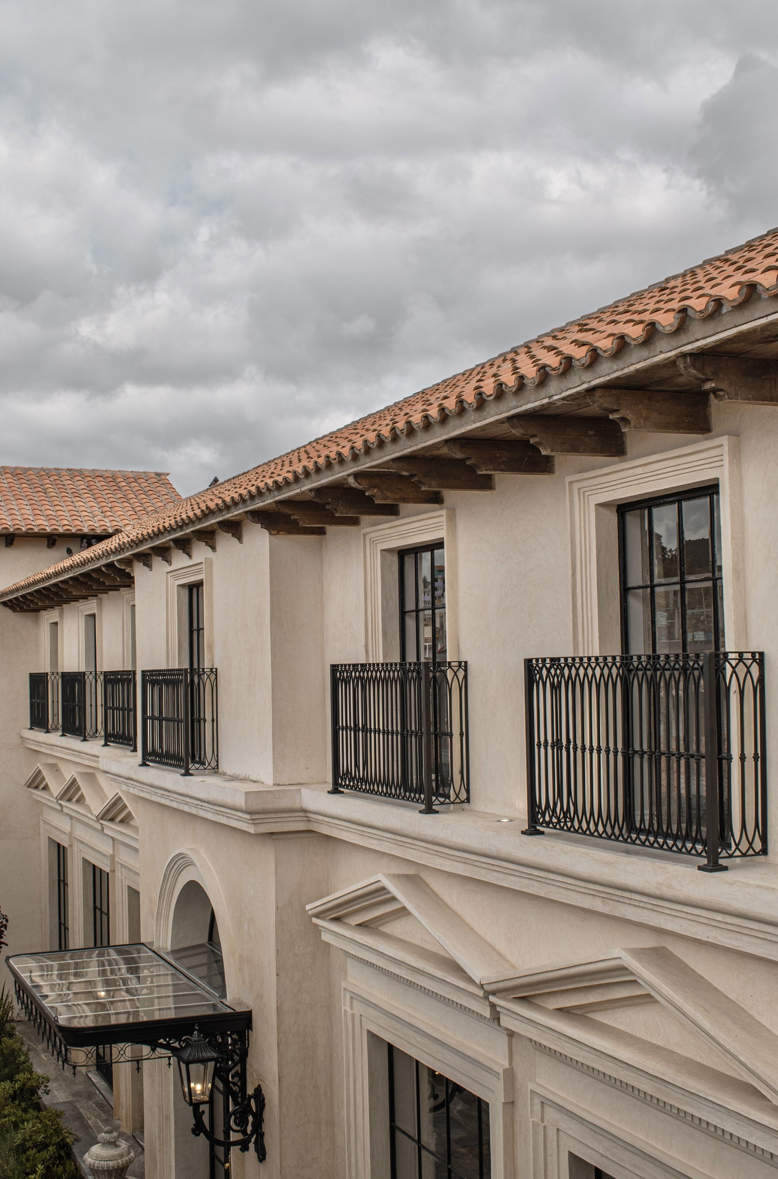 Un edificio de varios pisos con techo de tejas, balcones con barandillas de hierro forjado y ventanas amplias.