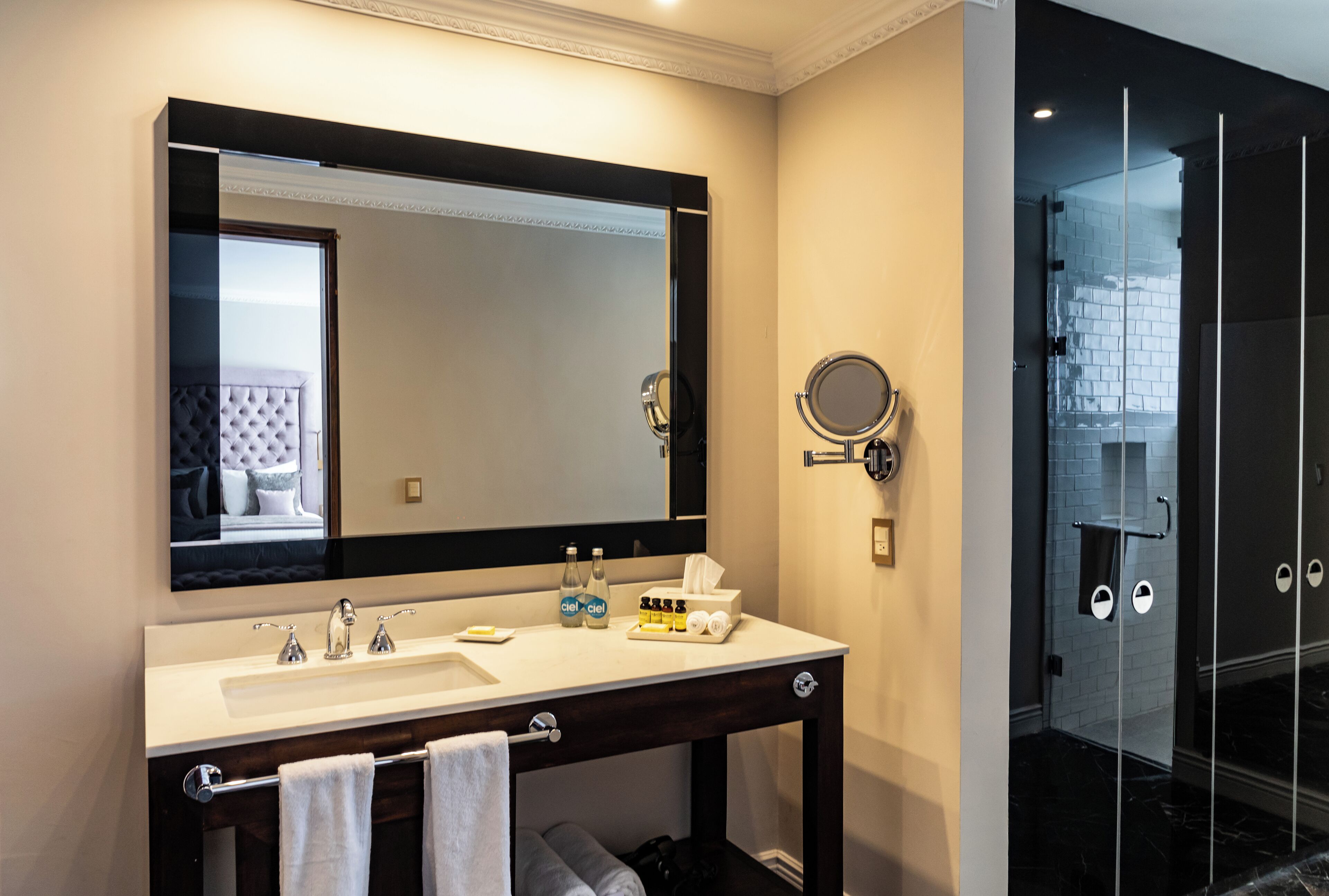 A modern bathroom with a large mirror, dual sinks, and a glass shower enclosure.