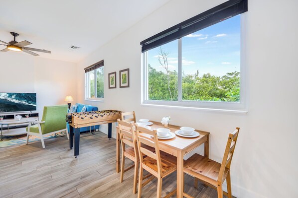 A dining area with a wooden table and chairs, a foosball table, and a television.