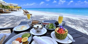 A beachside table with breakfast items, a pineapple cake, and a view of the ocean.