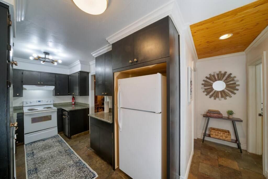 Eine moderne Küche mit dunklen Schränken, einem weißen Kühlschrank und einer Holzbalkendecke.