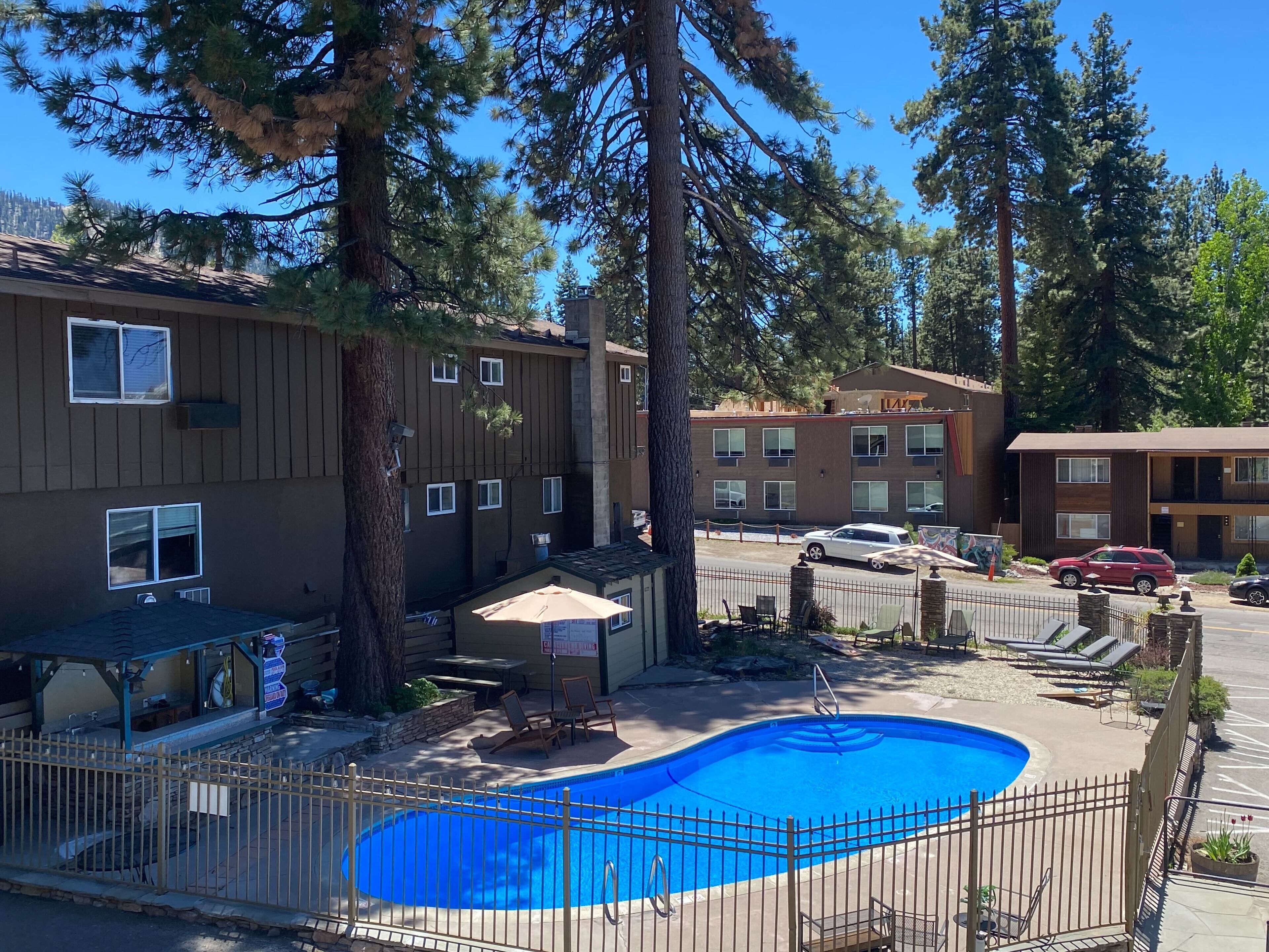 A hotel with a swimming pool, outdoor seating, and a parking area.