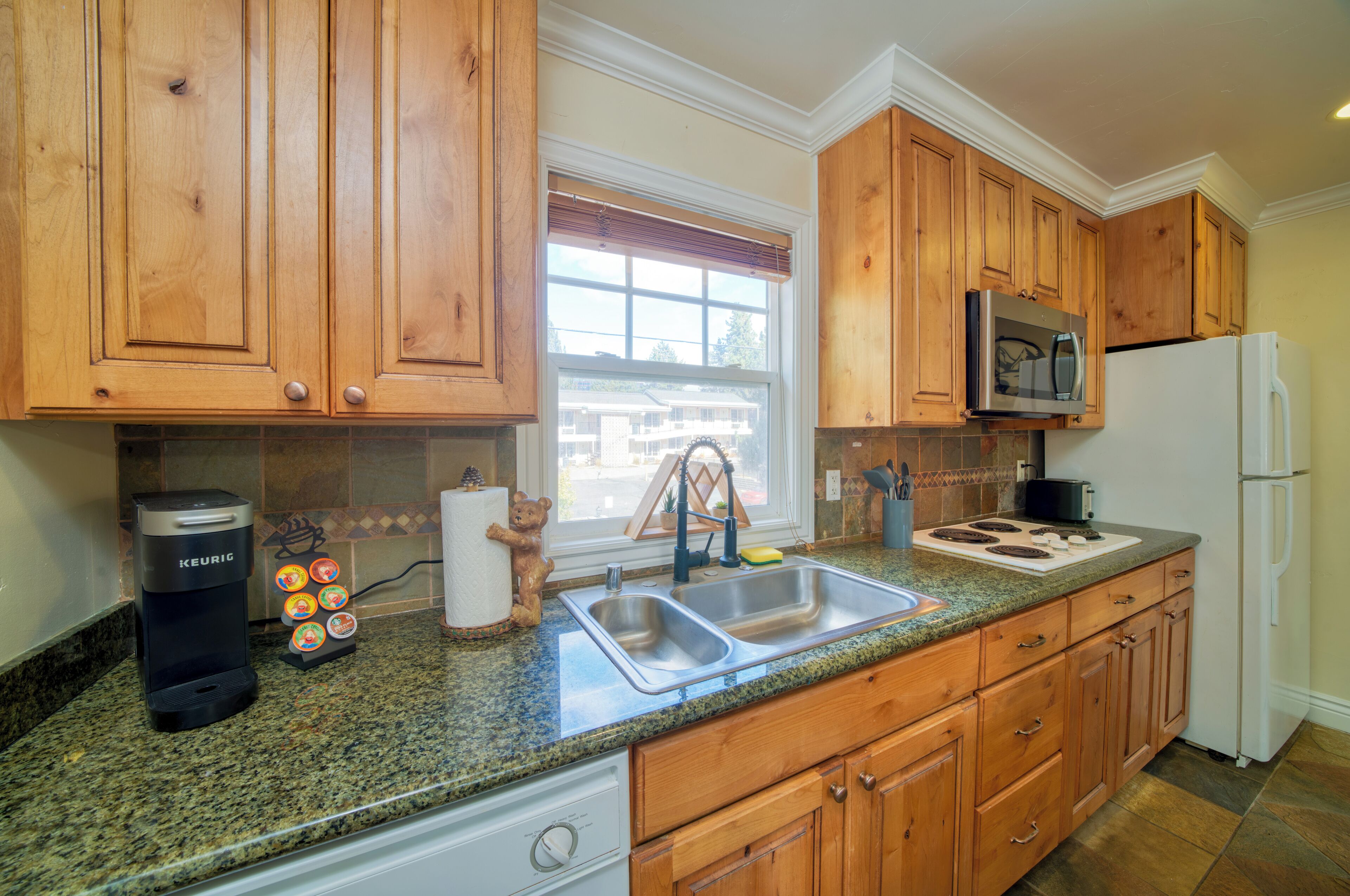 A kitchen with wooden cabinets, a stainless steel sink, a microwave, and a coffee maker.