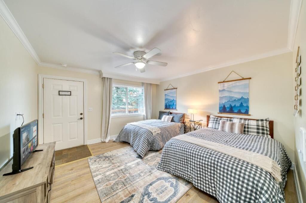 A bedroom with two beds, a ceiling fan, a TV, and artwork on the walls.