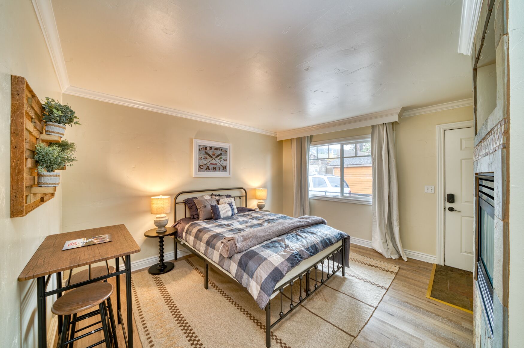 A bedroom with a bed, bedside tables, a small table with chairs, a window with curtains, and a door.
