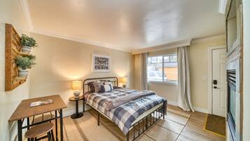 A bedroom with a bed, bedside tables, a small table with chairs, a window with curtains, and a door.