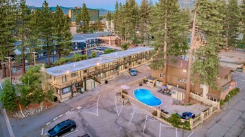 A hotel with a swimming pool, surrounded by tall trees and a parking lot.
