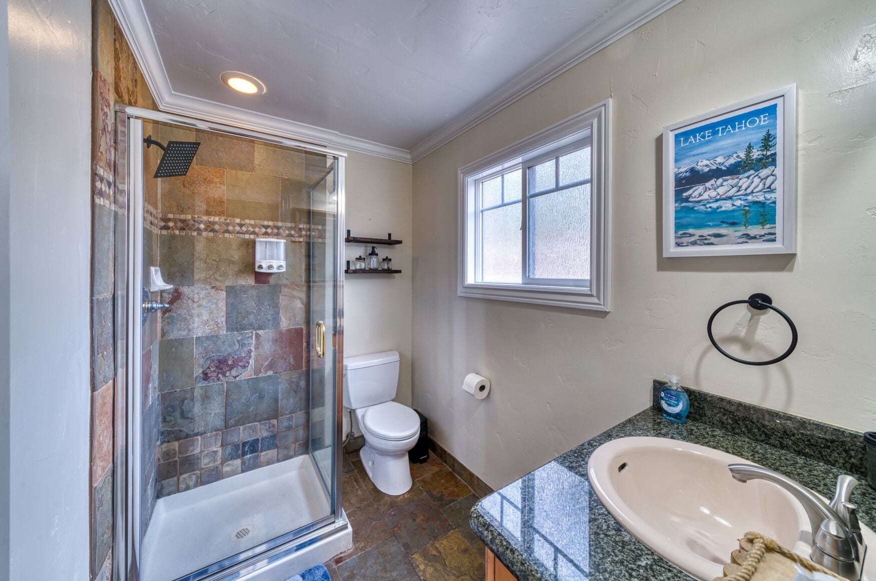 A bathroom with a glass-enclosed shower, a toilet, a sink, and a window.