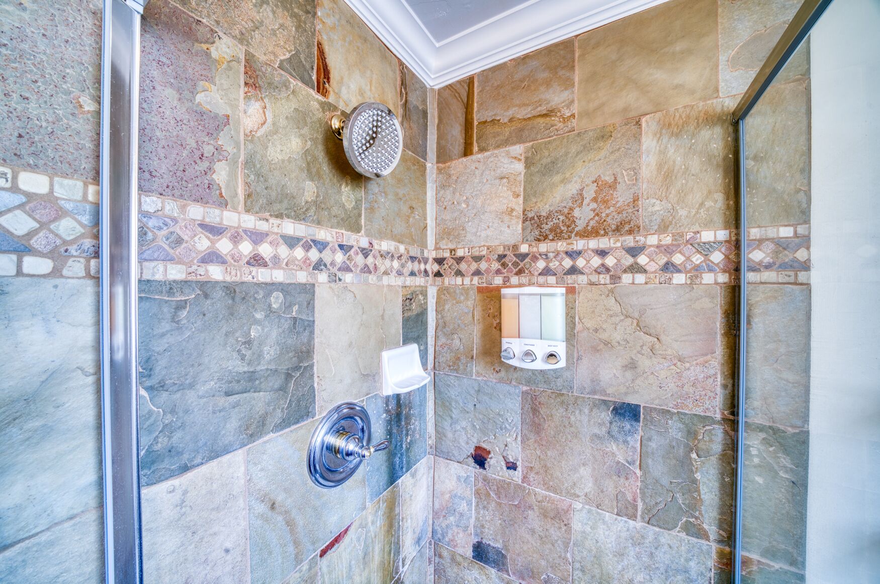 A shower with a glass door, a handheld showerhead, and a control panel.