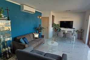 A modern living room with a blue accent wall, a sofa, a coffee table, and a dining area with chairs and a TV.