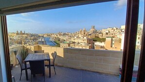 Un balcon avec une table et des chaises, donnant sur un paysage urbain avec des immeubles et une rivière.