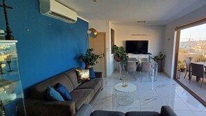 Un salon moderne avec un mur d’accent bleu, un canapé, une table basse et un coin repas comprenant des chaises et un téléviseur.