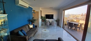 A modern living room with a blue accent wall, a sofa, a coffee table, and a dining area with chairs and a TV.