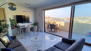 Un salon moderne doté d’une grande fenêtre, d’un téléviseur à écran plat, d’un coin repas et d’un balcon offrant une vue sur la ville.