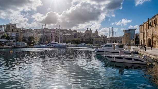 Un port de plaisance avec des bateaux amarrés, un ciel dégagé et des bâtiments en arrière-plan.