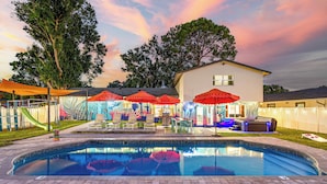 A swimming pool with a slide, surrounded by umbrellas and a mural.