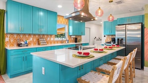 A modern kitchen with teal cabinets, a large island, stainless steel appliances, and pendant lighting.