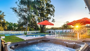 A hot tub area with two red umbrellas, a pool, and outdoor seating.