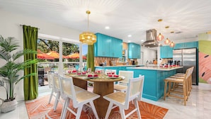 A modern kitchen with teal cabinets, a central island, and a dining area with white chairs and a wooden table.